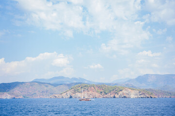 Fototapeta premium Scenic sailboat near mountainous coastline under partly cloudy sky on calm sea. 