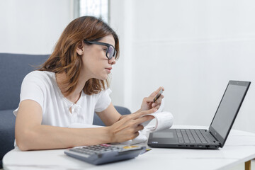 women managing finances at home, holding credit card and receipts while checking laptop, concept of...