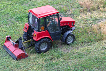 A tractor cutting weeds with a lawnmower on a field or lawn area, tractor work on weed cutting, tractor work with a lawnmower.
