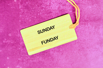 A light yellow tag with SUNDAY FUNDAY on it rests on a textured magenta surface, held by a string,...