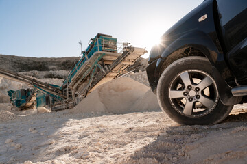 Black car with quarry equipment and stone crusher in operation on the background
