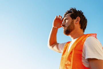 Construction worker looking into distance under bright sunlight, copy space