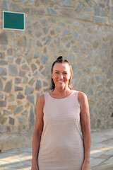 Portrait of a happy mature tourist woman standing in front of a stone wall in Spain