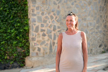 Portrait of a happy mature tourist woman standing in front of a stone wall in Spain