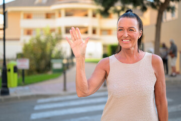 Happy mature tourist woman waving while looking away after crossing walking street in city in Spain