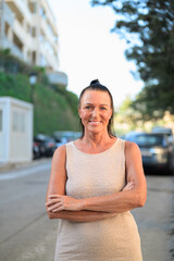 Portrait of happy mature woman standing with arms crossed in urban environment