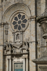 Obraz premium Cathedral facade with rose window, columns, sculpture, and green door. Historic architecture, sacred aesthetics, stone texture, Portugal.