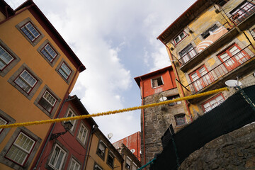 Upward view between colorful facades with garland, balconies, and satellite dishes. Domestic scene, festive accent, urban texture, Portugal.