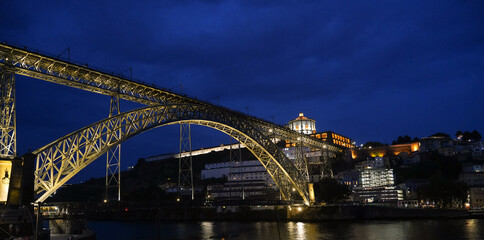 Naklejka premium Night view of Dom Luís I Bridge in Porto with illuminated Serra do Pilar Monastery. Historic engineering, urban depth, cultural scene, Portugal.