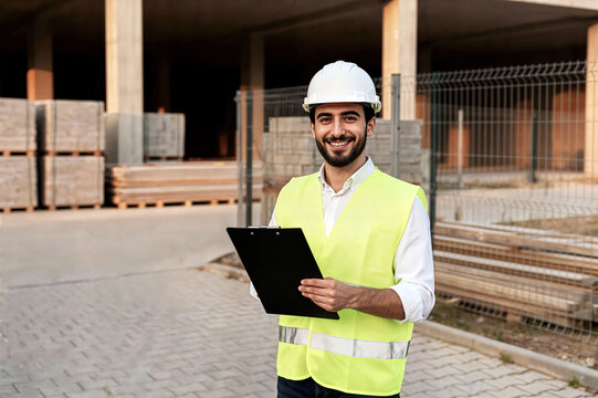 young man architect wearing safety vest helmet holding tablet smiling construction site Joven arquitecto con chaleco de seguridad y casco sosteniendo una tableta y sonriendo en una obra