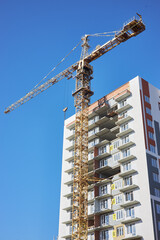 tall construction crane stands beside a newly developed high-rise building. Workers are busy as they continue construction, visible balconies showing progress