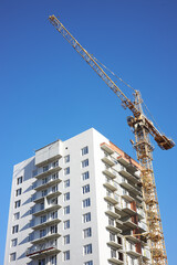 construction crane is positioned beside a tall building under construction. Workers can be seen on the site, preparing for the next stages of the project on a sunny day