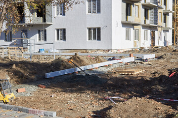 Workers are preparing the ground at a construction site where large concrete slabs are being laid for new residential buildings during the fall season. Trees show autumn leaves
