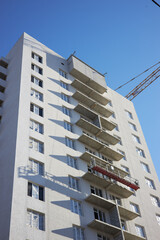 Workers carry out construction on the exterior of a high-rise building. Scaffolding is visible, and the sky is clear and blue, indicating a sunny day