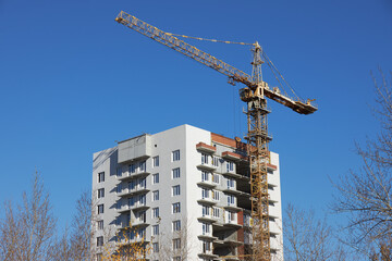 construction site shows a large yellow crane next to a modern building. clear blue sky provides a bright backdrop for the unfolding urban development