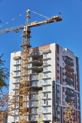 construction site featuring a tall residential building being completed. large crane is positioned, lifting materials on a sunny day with no clouds in the sky