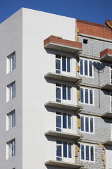 exterior of a residential building under renovation shows a mix of completed and unfinished sections. Bright sunlight highlights the modern design and balconies
