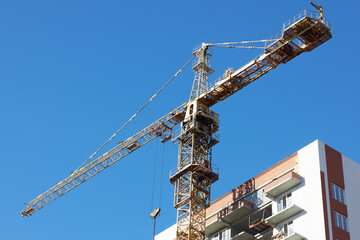 tall construction crane is positioned near a modern building. bright blue sky provides a clear backdrop, highlighting the ongoing construction activity in the city