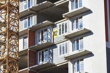 high-rise construction site features concrete floors with framed windows and a large number marking on one level. crane stands nearby under a clear sky