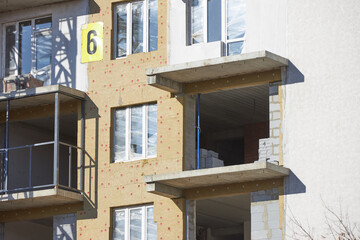 New residential building under construction features exposed walls and open windows. Scaffolding surrounds the structure, indicating ongoing work and improvement in the area
