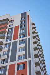 tall apartment building showcases modern architecture with colorful accents on its exterior. structure stands against a bright blue sky, highlighting its design and vibrant colors