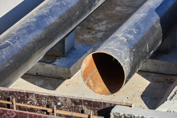 Steel pipes are positioned on a concrete base at a construction site. sun shines brightly, highlighting the rough texture of the materials and surrounding area