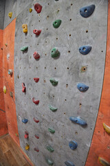 climbing wall displays various colorful holds positioned at different heights. wall is part of an indoor rock climbing gym, capturing a moment of activity and excitement
