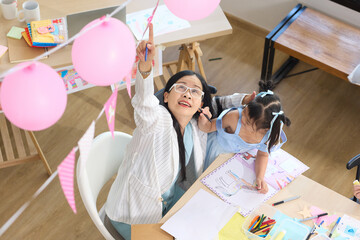 A teacher points upward while drawing on a paper with children. They are engaged in an art lesson together, smiling and having fun