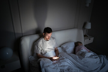Weary man awake scrolling smartphone late night unable to sleep in bedroom with wife. Insomnia issue, nighttime procrastination, digital distraction, sleep problem, mental restlessness, health concern
