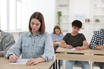 Students taking exam at wooden table indoors, selective focus