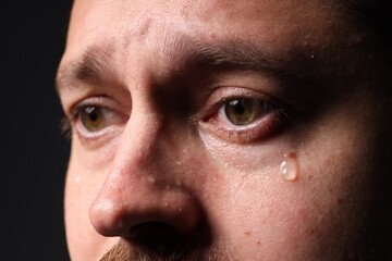 Obraz premium Sad man crying on black background, closeup