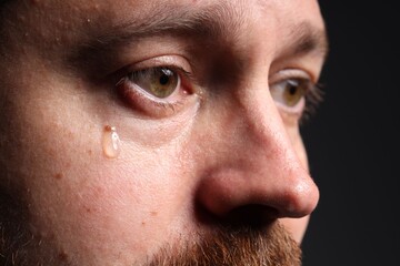 Fototapeta premium Sad man crying on black background, closeup