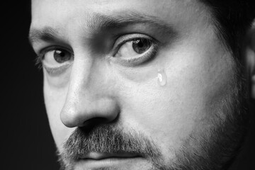 Obraz premium Sad man crying on dark background, closeup. Black and white effect