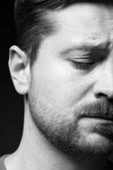 Obraz premium Sad man crying on dark background, closeup. Black and white effect