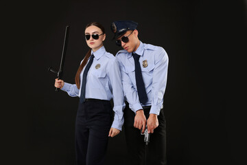 Young policewoman and policeman on black background