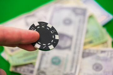 Black poker chip held over US dollar bills.