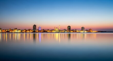 Naklejka premium Vibrant Cityscape Reflection A Serene Evening Panorama of Illuminated Buildings and a Mosque on Calm Waters at Dusk