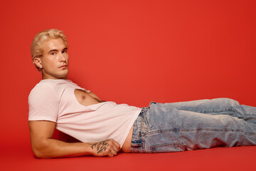 Stylish young man lounging against a vibrant red backdrop with confident allure