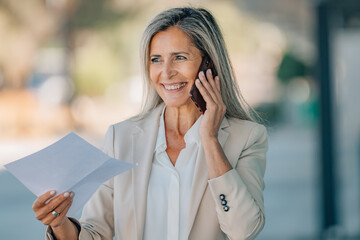 attractive middle-aged adult woman with bill or document talking on the phone on the street