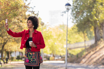 Fototapeta premium young latina woman on the street with a cell phone and a cup of drink
