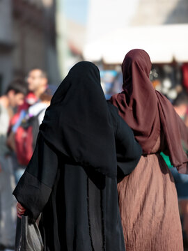 Two Muslim women walk on their bacl in the city center, in the background poeple and buildings in soft focus