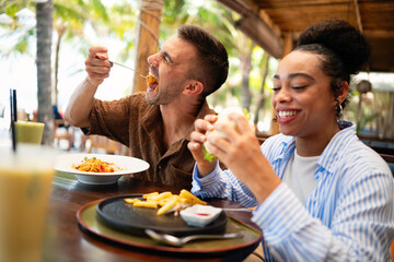 Happy diverse couple enjoying food at the restaurant, indulging in the guilty pleasure of fast food