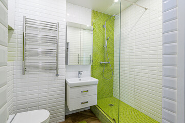 A compact bathroom with white subway tiles, green mosaic shower, and a vanity with a mirror. A...