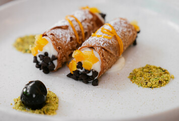 Italian cannoli dessert with ricotta cream, chocolate chips, and orange zest on a white plate
