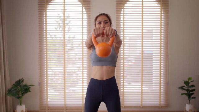 Adult Asian woman performs kettlebell workout at home for strength and fitness achieves healthy lifestyle