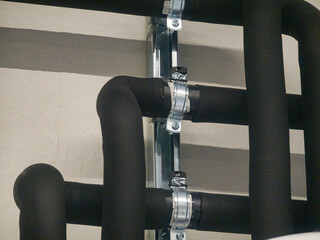 Black insulated pipes secured with metal clamps in an industrial setting