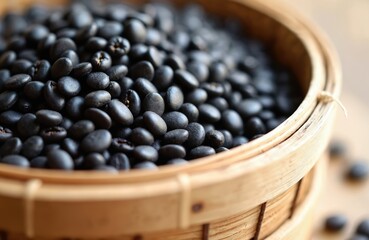 Close up of dried black beans inside a round bamboo sieve. Dark beans are piled high in the basket. Some beans spill onto the blurred background surface.
