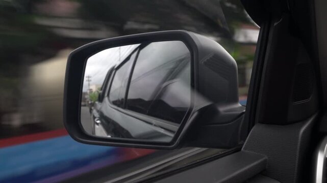 Car side mirror reflecting road and surroundings while driving.