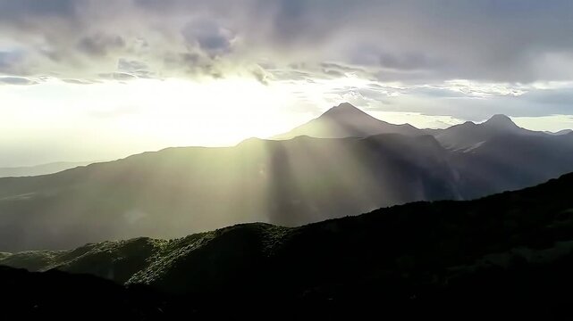 Breathtaking mountain landscape with dramatic sun rays shining through clouds illuminating silhouetted peaks and valleys in an inspiring and serene natural vist