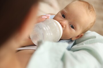 Mother feeding her newborn baby with bottle at home, closeup